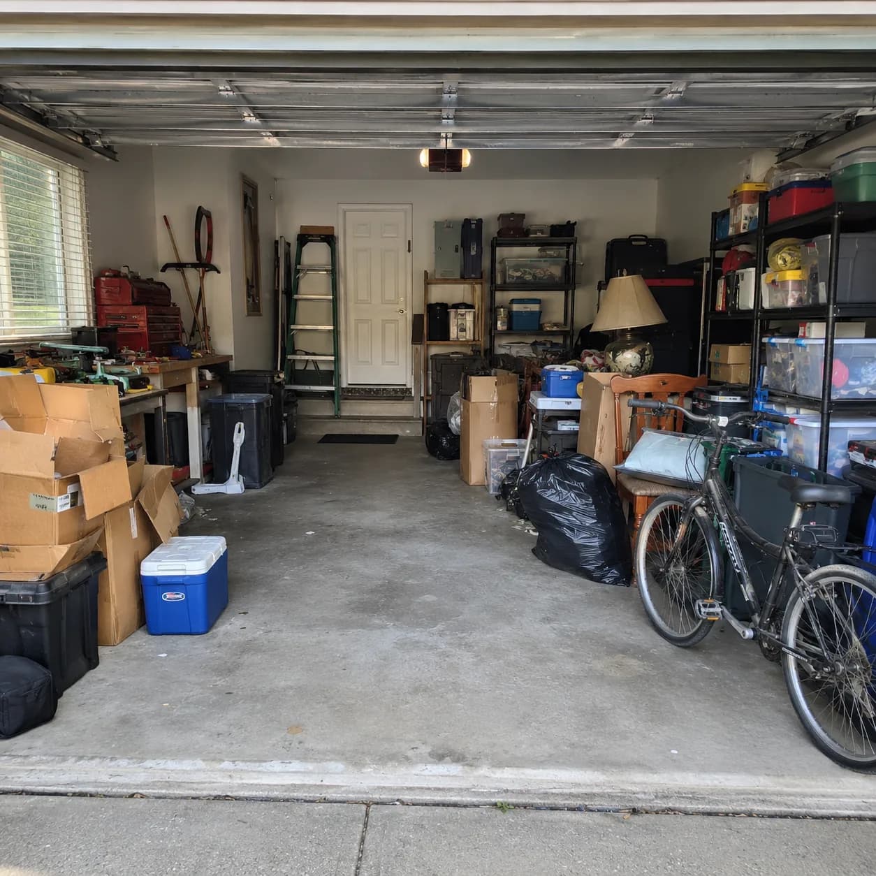 A two-car garage packed wall to wall with boxes, shelving, tools and a bicycle, leaving no room to park.